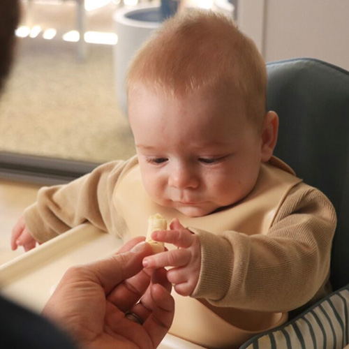 Baby who has just started eating reaching out at piece of banana